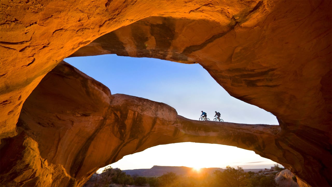 Cycling across a natural rock arch in the desert near Moab, Utah (© Whit Richardson/Cavan)