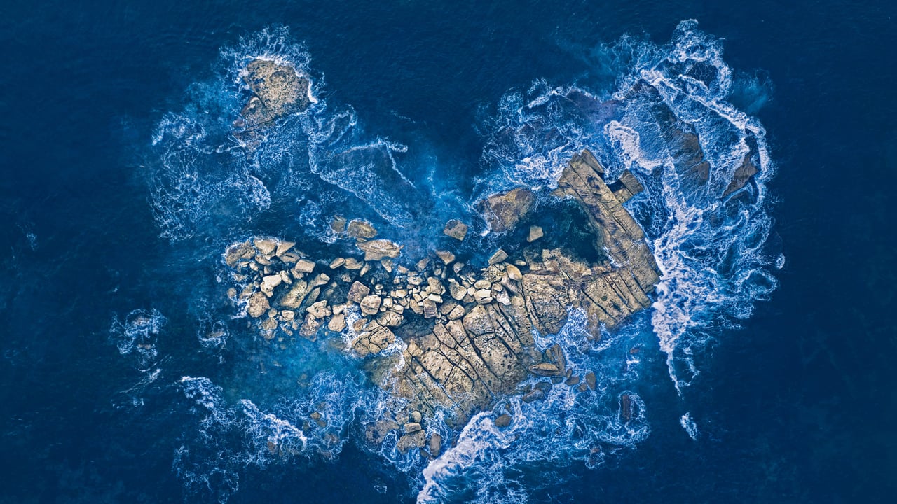Ocean waves crashing over a heart-shaped rock island off the coast of Sydney, Australia (© Kristian Bell/Getty Images)