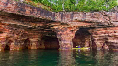 Bing wallpaper August 4, 2019. Kayaker exploring sandstone sea caves in Apostle Islands National Lakeshore, USA (© Chuck Haney/Danita Delimont)
