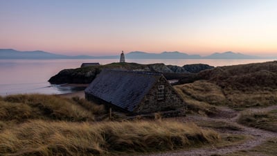 Bing wallpaper January 13, 2025. Cottage with Tŵr Mawr Lighthouse in the background, Ynys Llanddwyn, Wales (© Westend61 on Offset/Shutterstock)