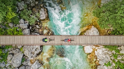 Bing wallpaper June 3, 2021. Cyclists on a wooden suspension bridge over the Soča River in Slovenia (© Amazing Aerial Agency/Offset by Shutterstock)