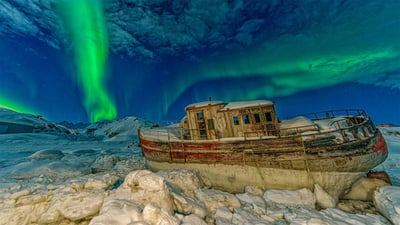 Bing wallpaper January 13, 2022. Northern lights over a stranded boat in Tasiilaq, Greenland (© Shane P. White/Minden Pictures)